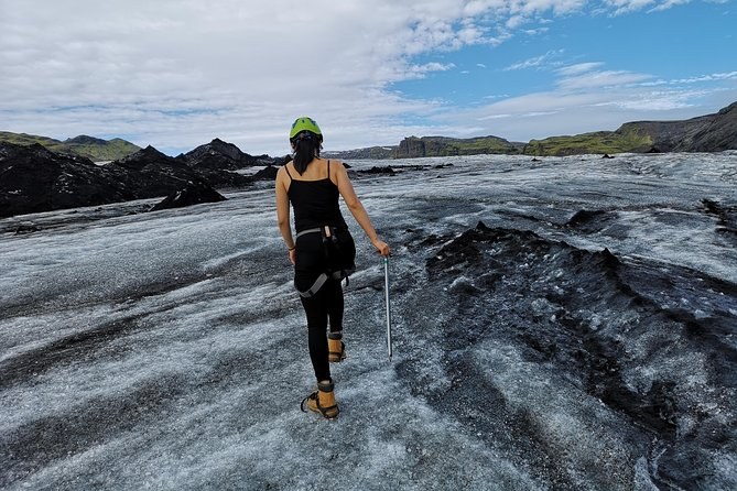A hiker in crampons walking away across grey ash-banded glacier ice