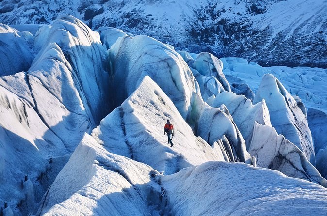 Steep blue ice ridges and crevasses, one climber small in the middle of them