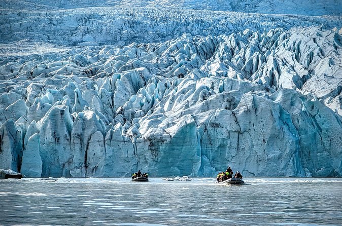 Two small boats on the water below a towering crevassed ice front