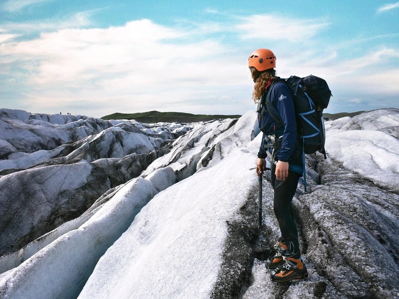 A helmeted hiker in crampons standing on ridged grey and white glacier ice