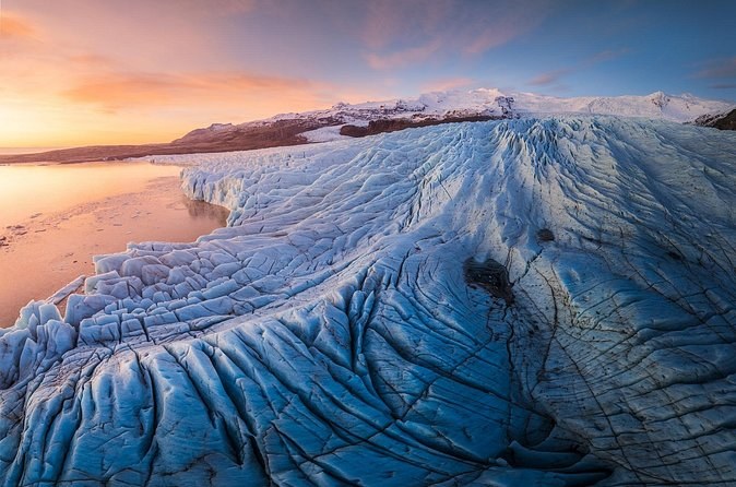 A crevassed outlet glacier running down to a lagoon under an orange evening sky