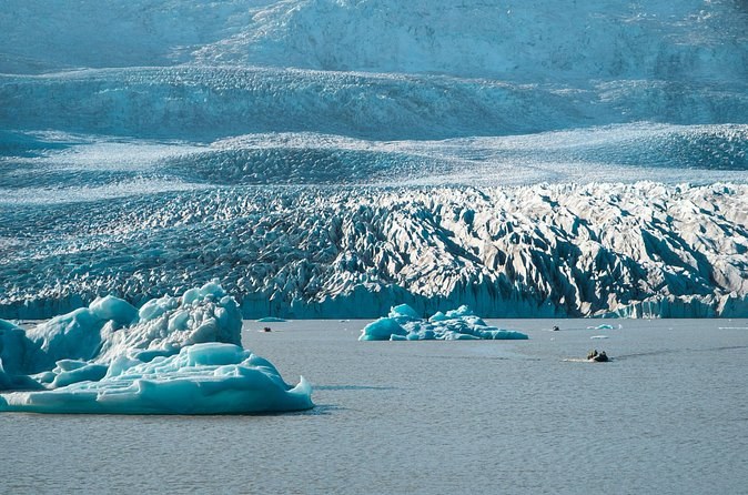 A crevassed glacier tongue meeting a grey lagoon, icebergs floating in front