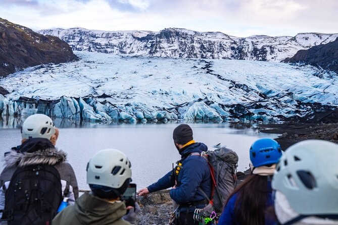 A guide briefing a helmeted group at the lagoon below a crevassed glacier tongue