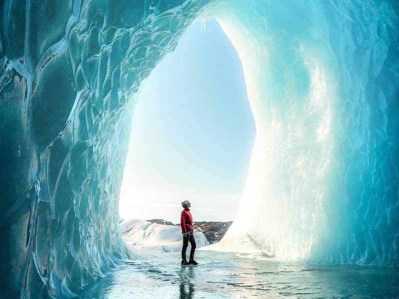 A tall ice arch opening onto daylight, a visitor standing in its mouth