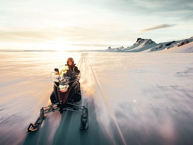 A snowmobile crossing a flat ice cap in low sun, its track running behind it