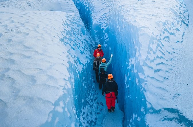 Hikers walking single file along the floor of a narrow blue crevasse